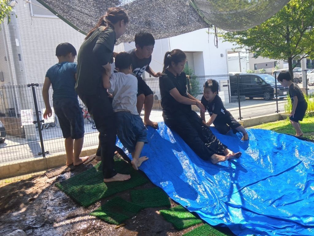 ブルーシートが敷かれた築山に、大人と子どもたちが登って滑り降りようとしている