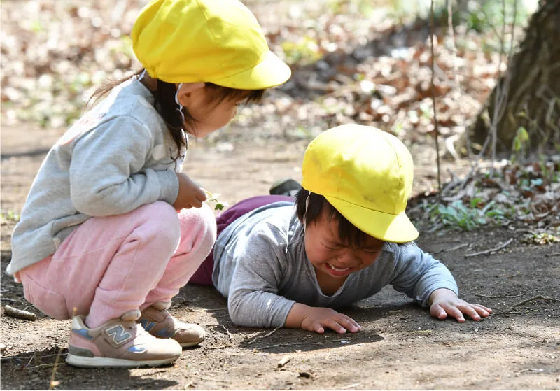 A child lying on the ground while another child watches nearby
