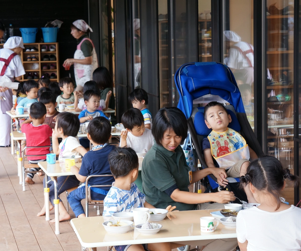 Children eating together while a staff member supports a child using a wheelchair