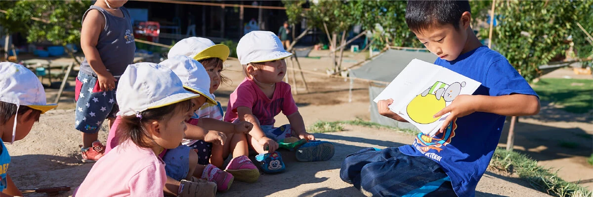 An older child reading a picture book to younger children