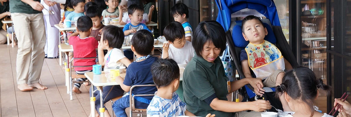 Children eating together while a staff member supports a child using a wheelchair