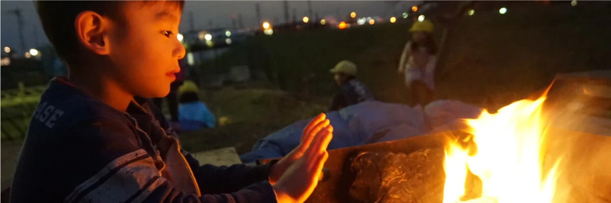 A child warming their hands by a bonfire