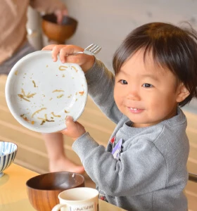 A child smiling while holding an empty plate after lunch