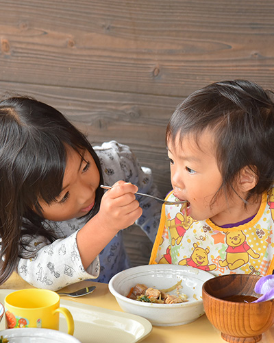 年上の子どもが年下の子どもに食事を食べさせる様子