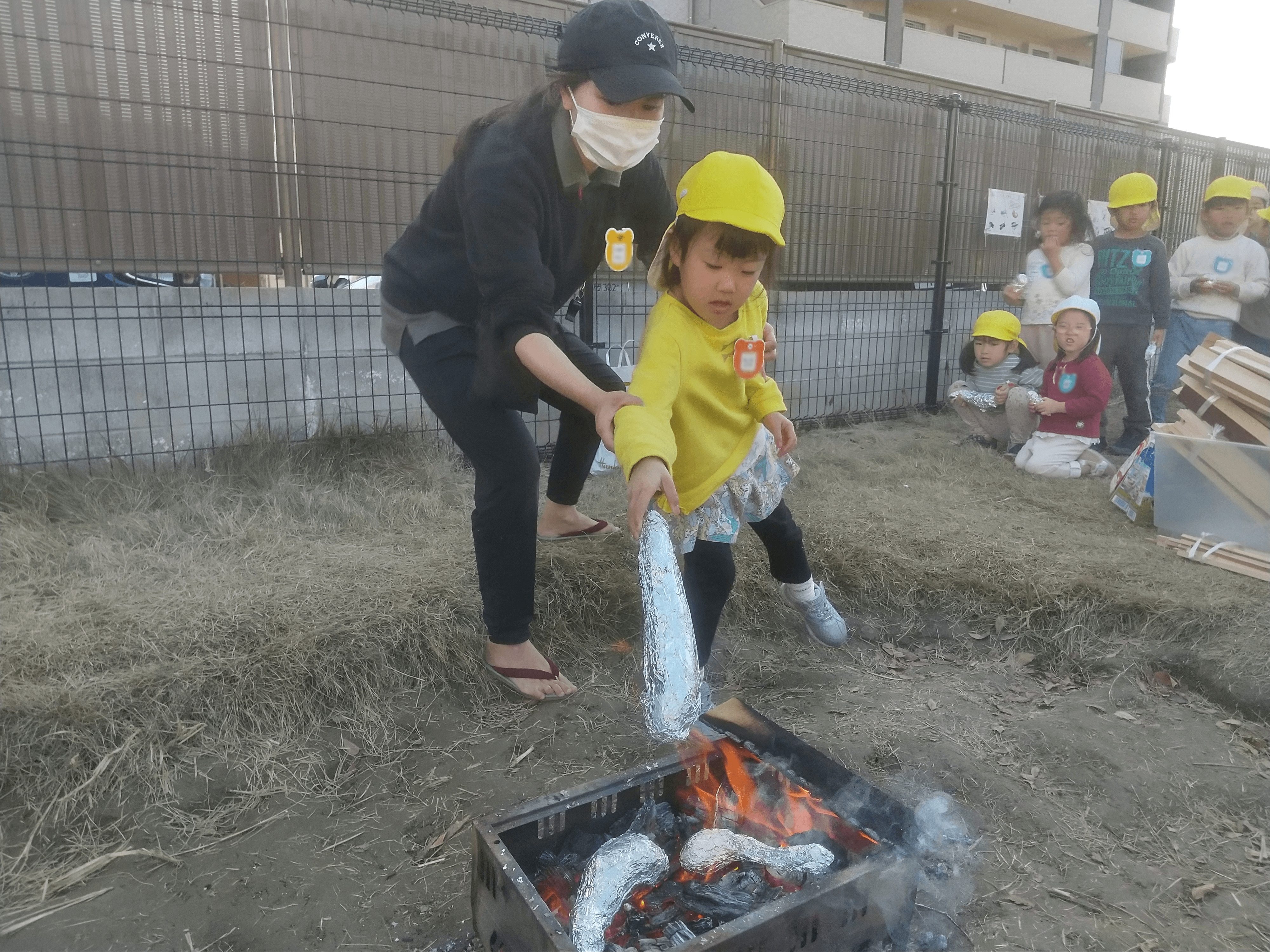焚き火に芋を入れる子ども