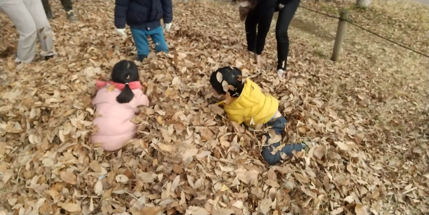 集めた落ち葉で遊ぶ子どもたち