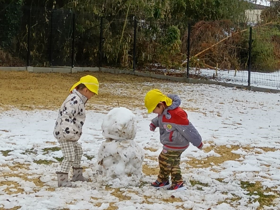 園庭で雪だるまを作り遊ぶ子どもたち