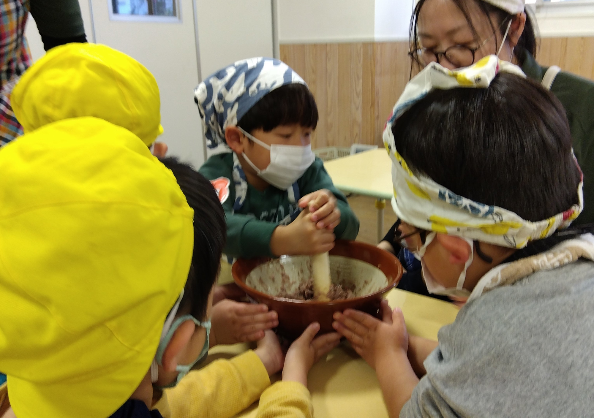 すり鉢で魚をすりつぶす子どもと、すり鉢を押さえる子どもたち