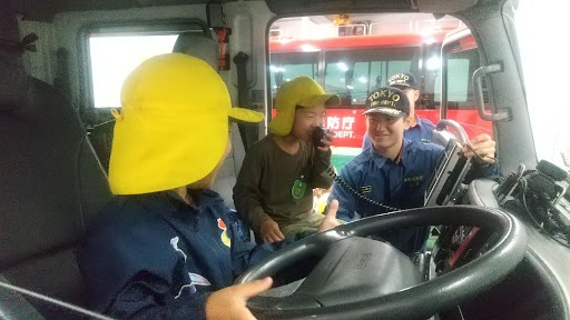 消防車に乗せてもらい、マイクを使って消防士の真似をする子どもたち