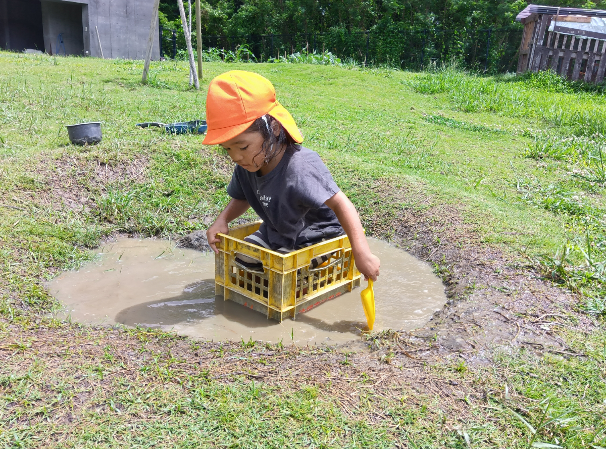 水たまりの中でカゴに入って遊ぶ子ども