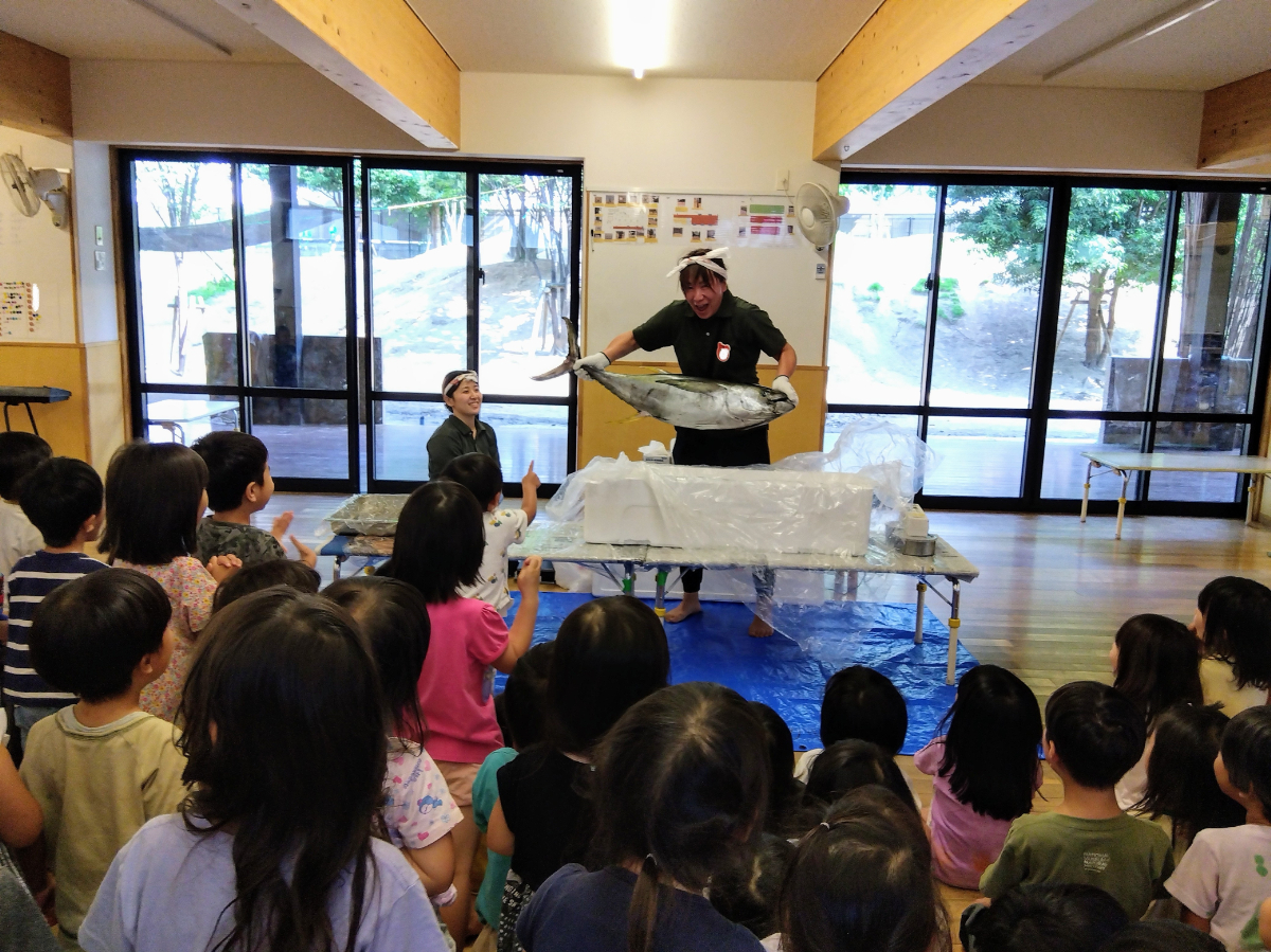 子どもたちの前でマグロを持ち上げる施設長