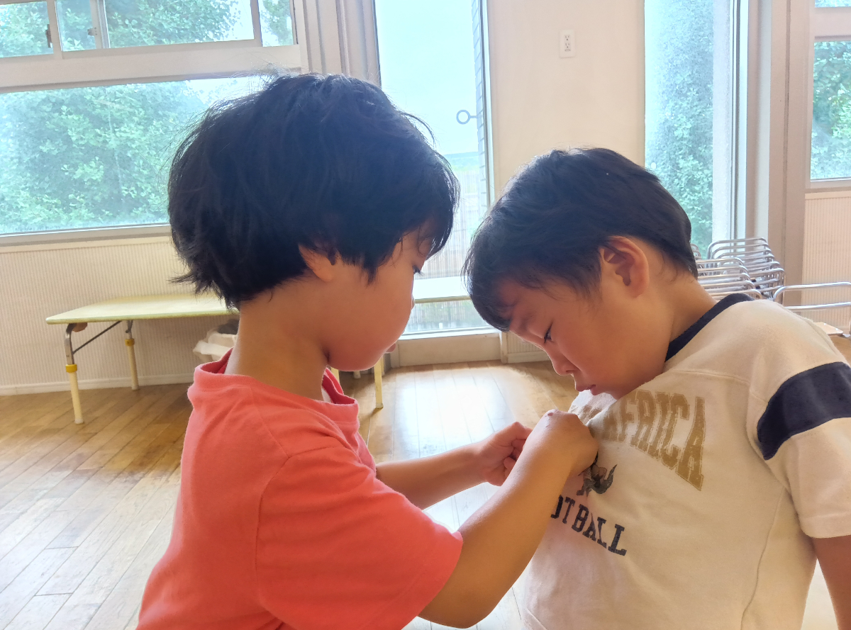 友だちの名札をつけるのを手伝う子ども