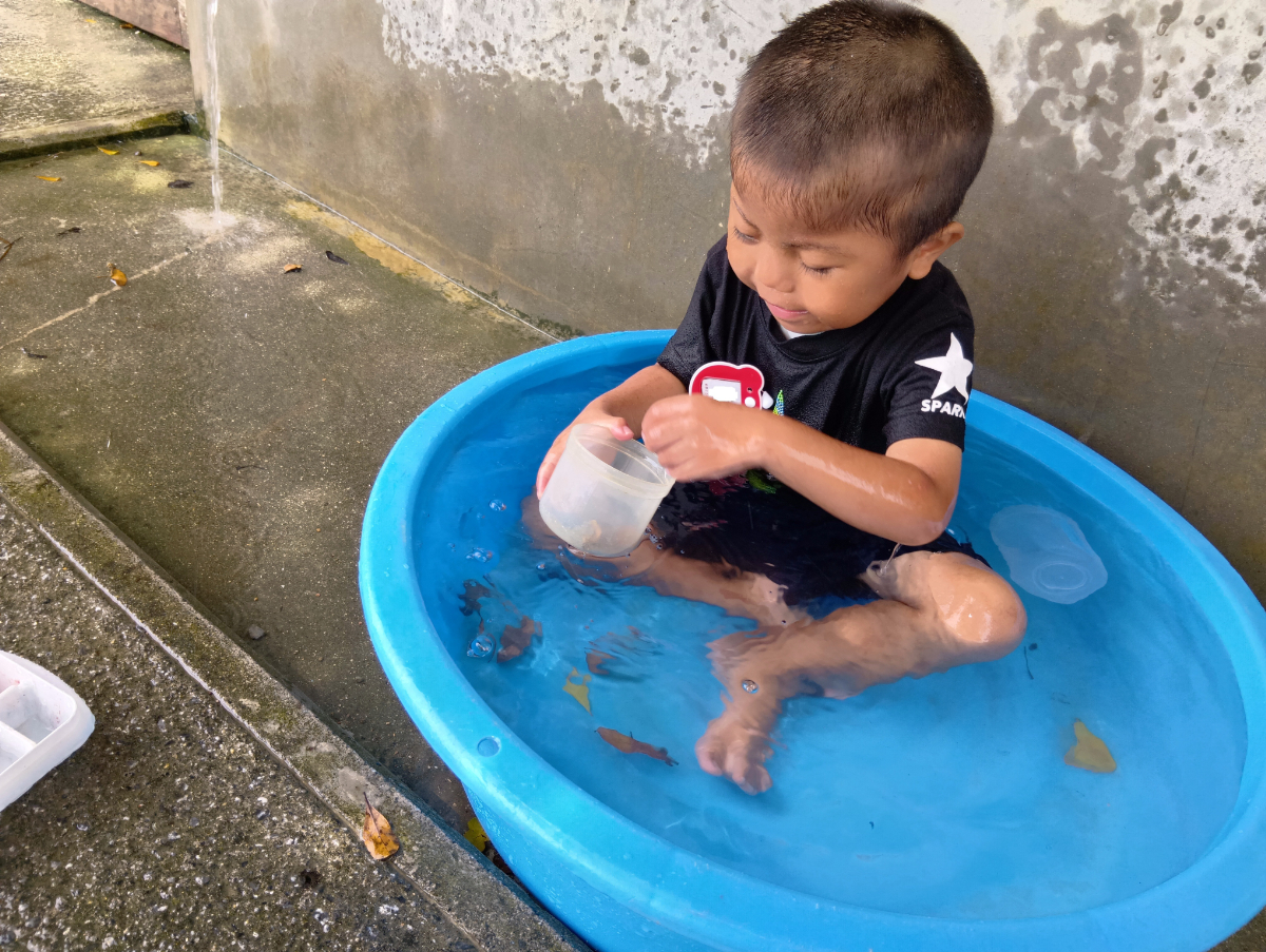 たらいに入れた水の中でで落ち葉すくいをする子ども