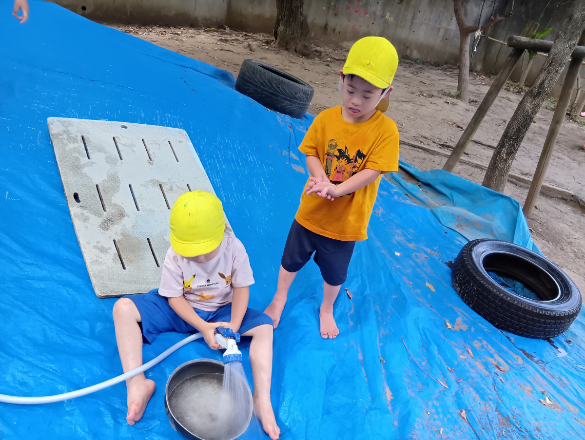 シャワーホースを使っている子どもに貸してと伝える子ども