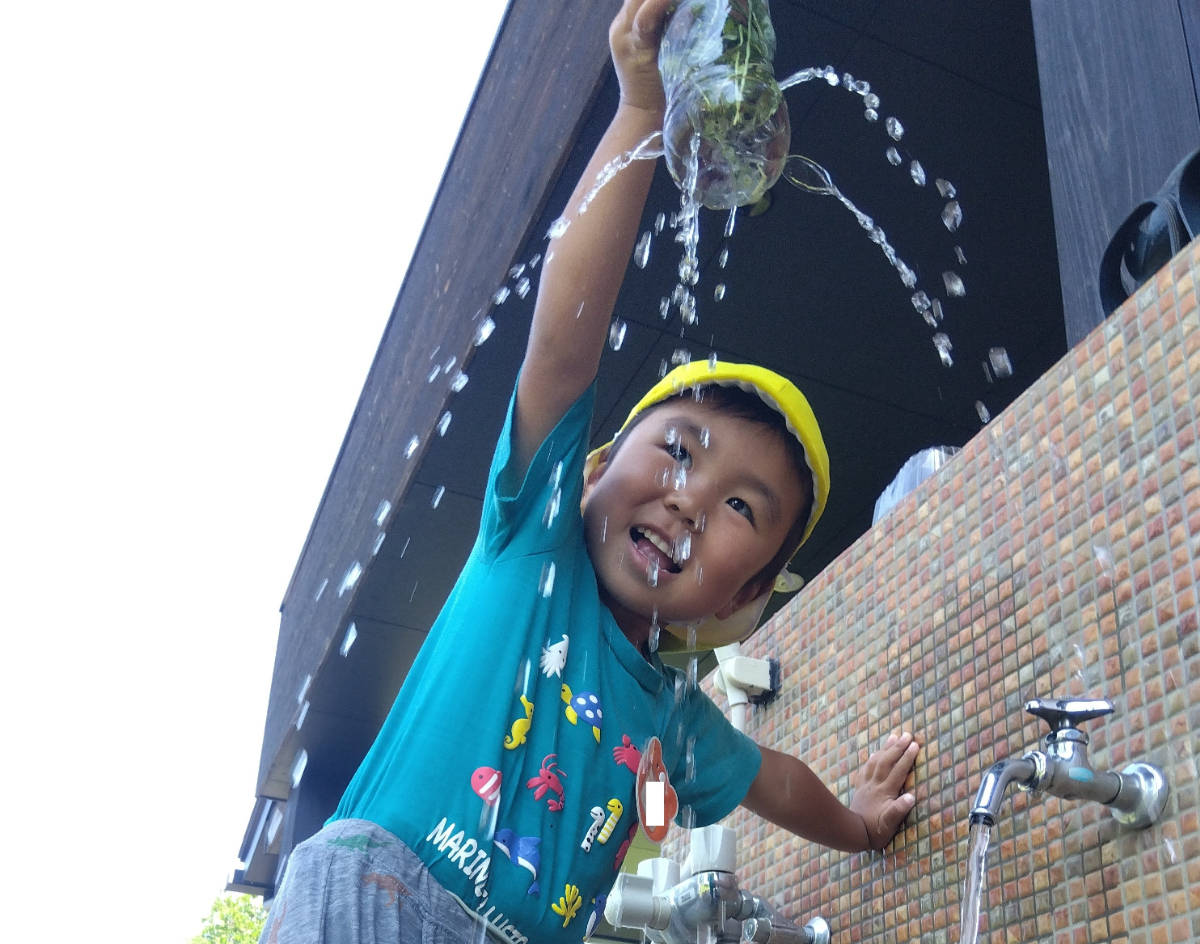 穴あきペットボトルから垂れてくる水で遊ぶ子ども
