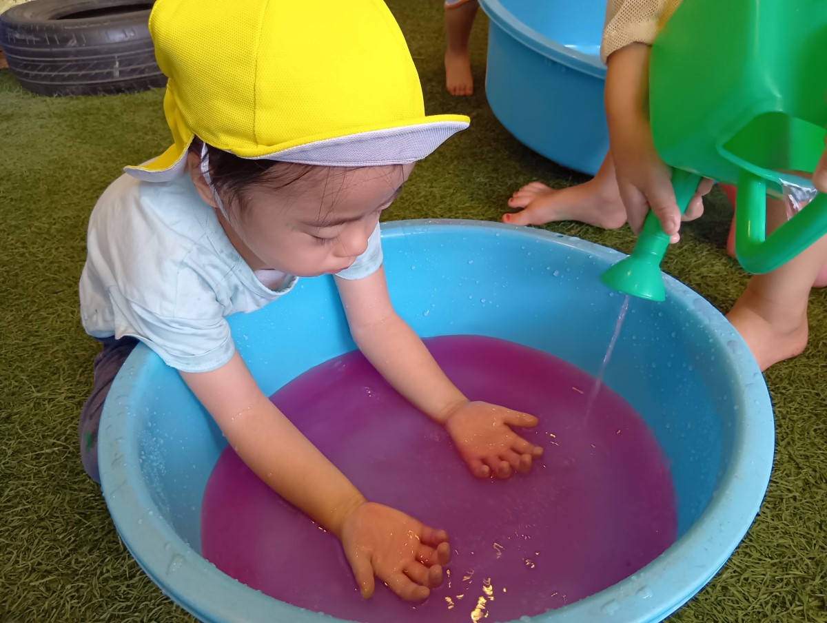たらいに入れた水で遊ぶ子ども