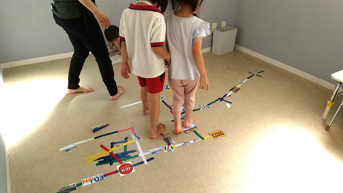 床にテープやスクラップを貼って町をつくる子どもたち