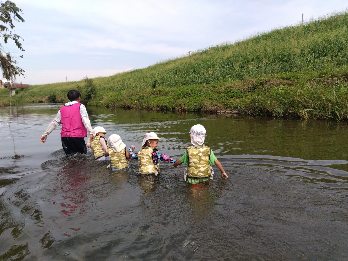手をつないで川の中を歩く子どもたち