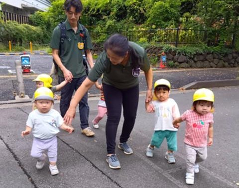 保育者と手を繋いで歩く乳児たち