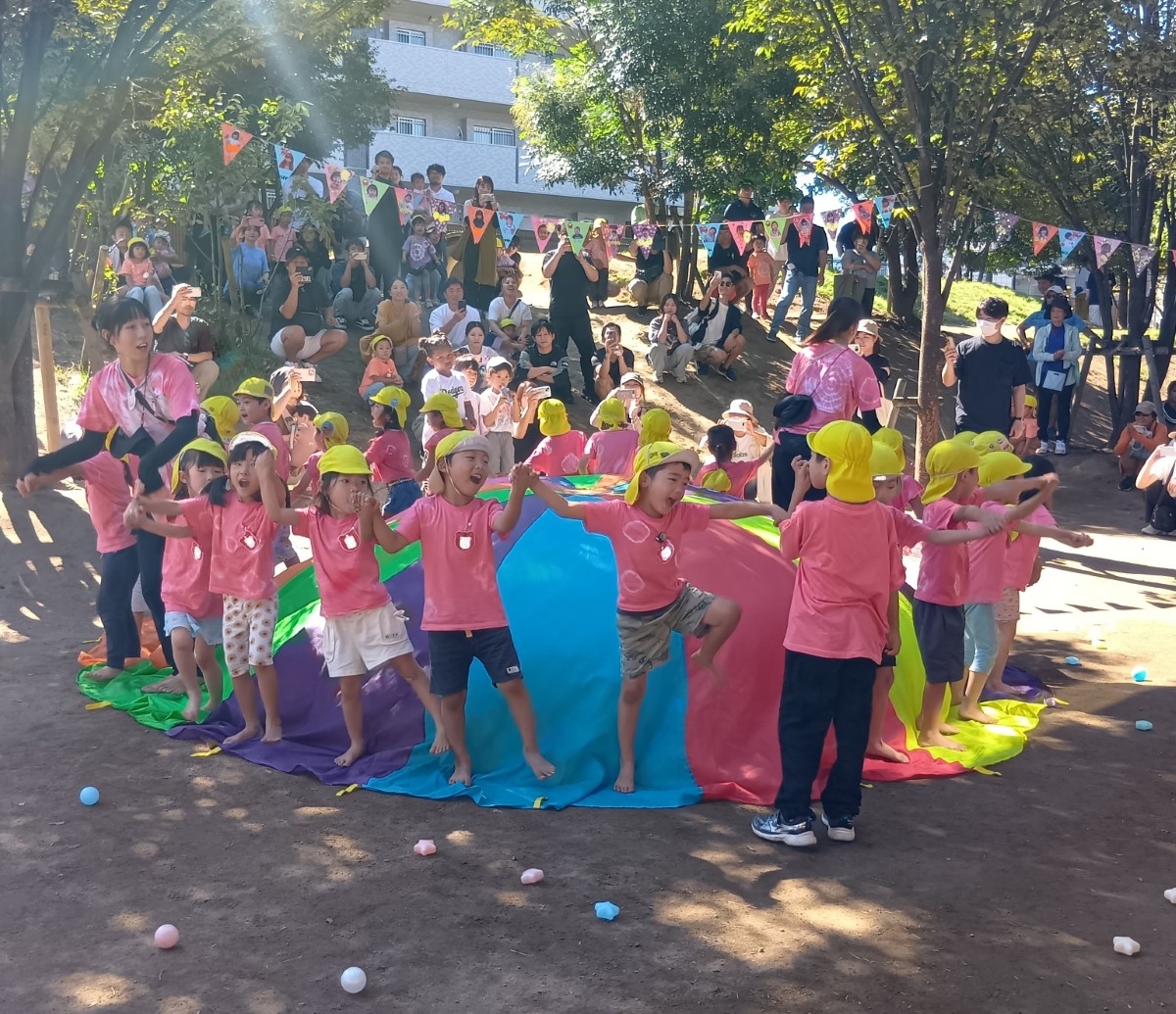 パラバルーンの周りで手をつないで踊る子どもたち