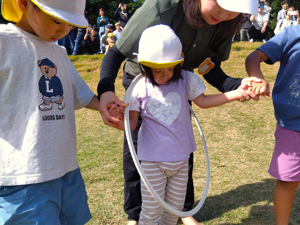 手をつないだまま、体に通されたフラフープを渡す子どもたち