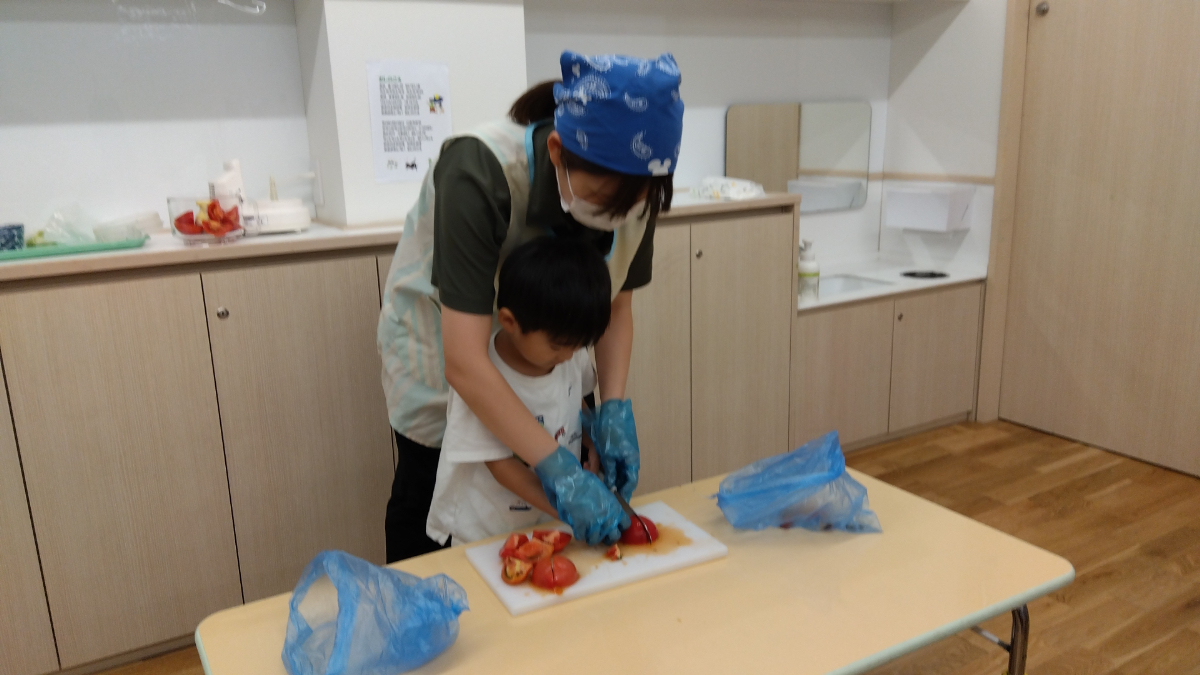 保育者と一緒にトマトを包丁で切る子ども