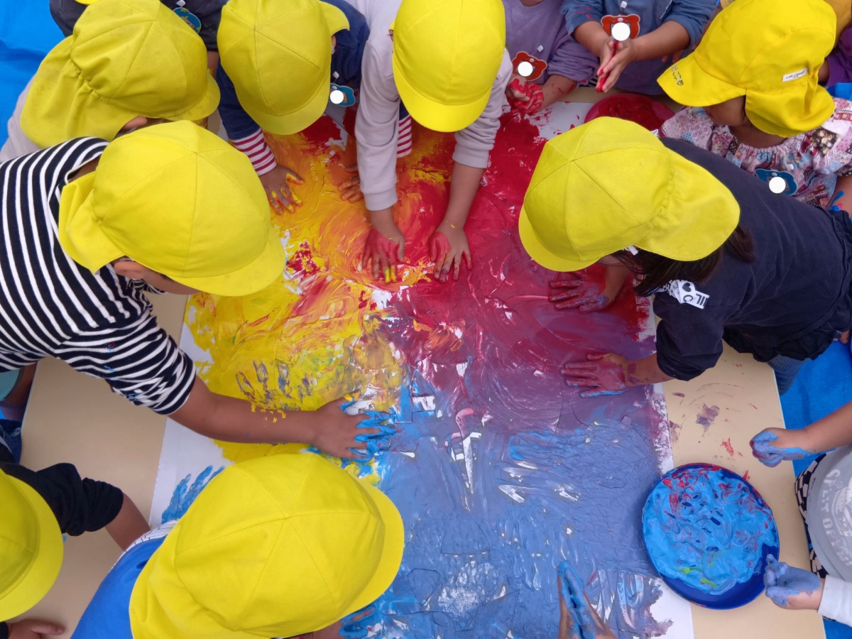 模造紙の上で絵の具を手でのばす子どもたち