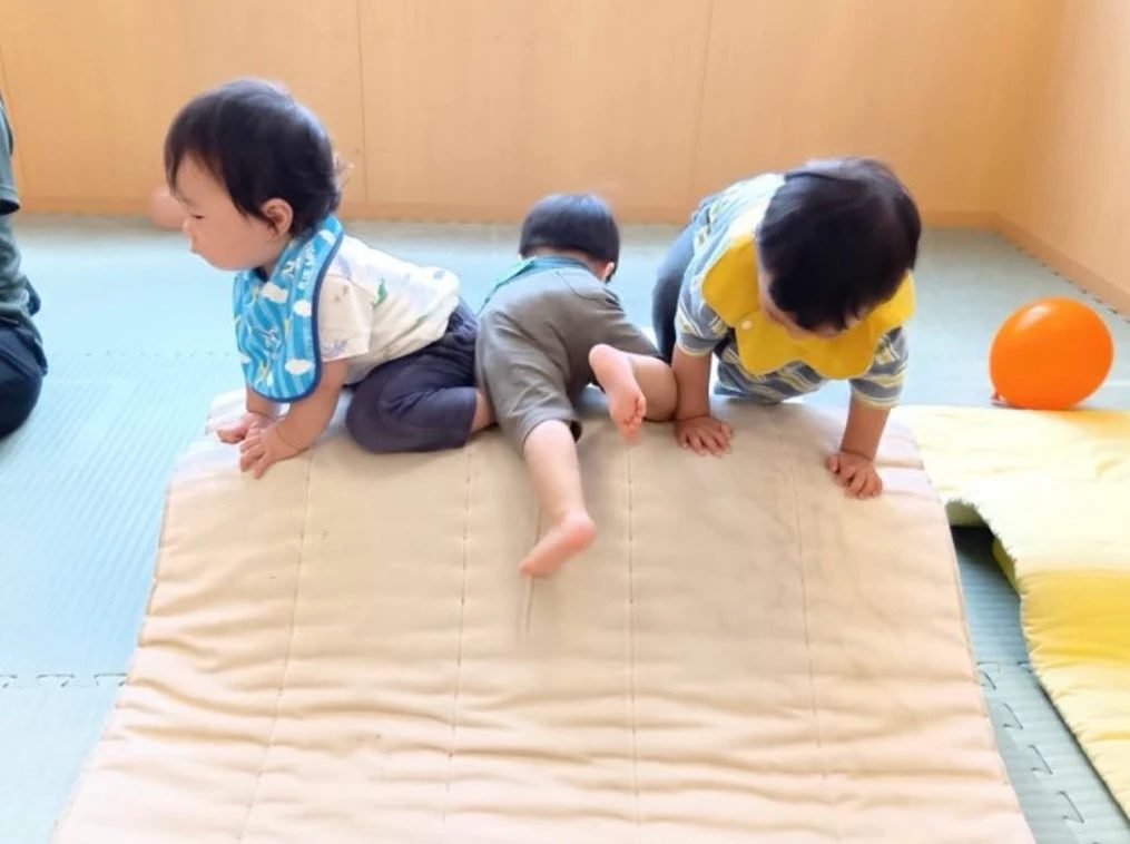 ハイハイでマットの山に登る子どもたち
