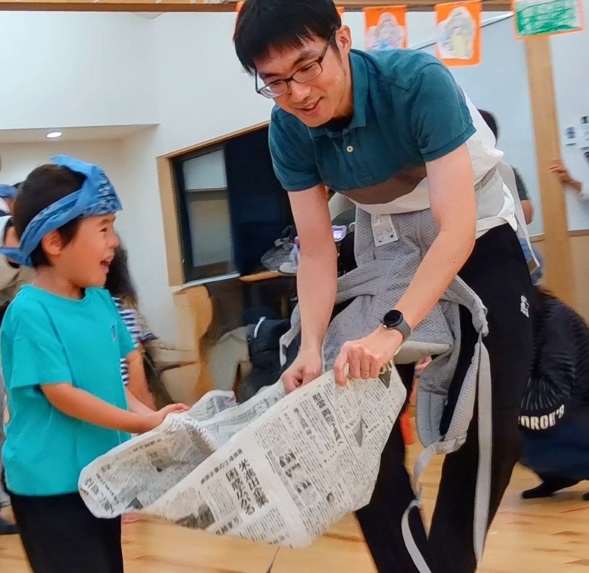 スタッフと一緒に新聞紙を持つ子ども
