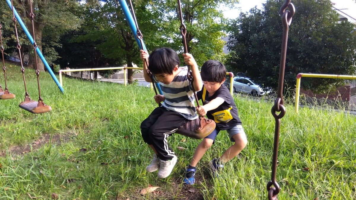 ブランコに乗る子どもと、漕ぐのを手伝う子ども