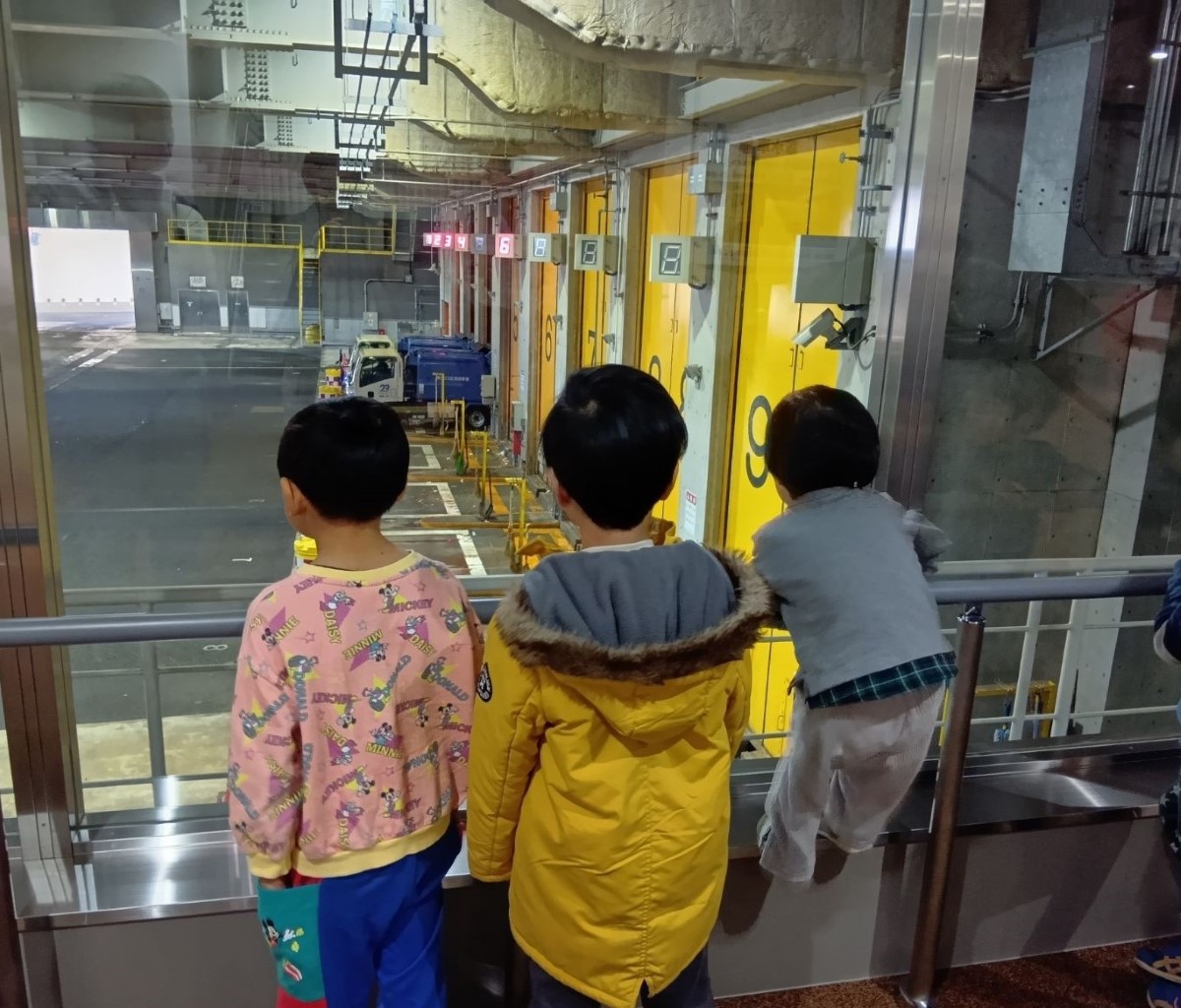 ゴミ収集車の到着を眺める子どもたち