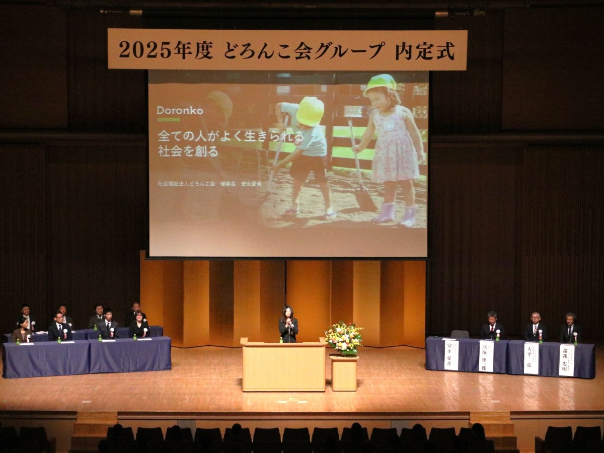 壇上のスライドを背景に祝辞を述べる安永理事長