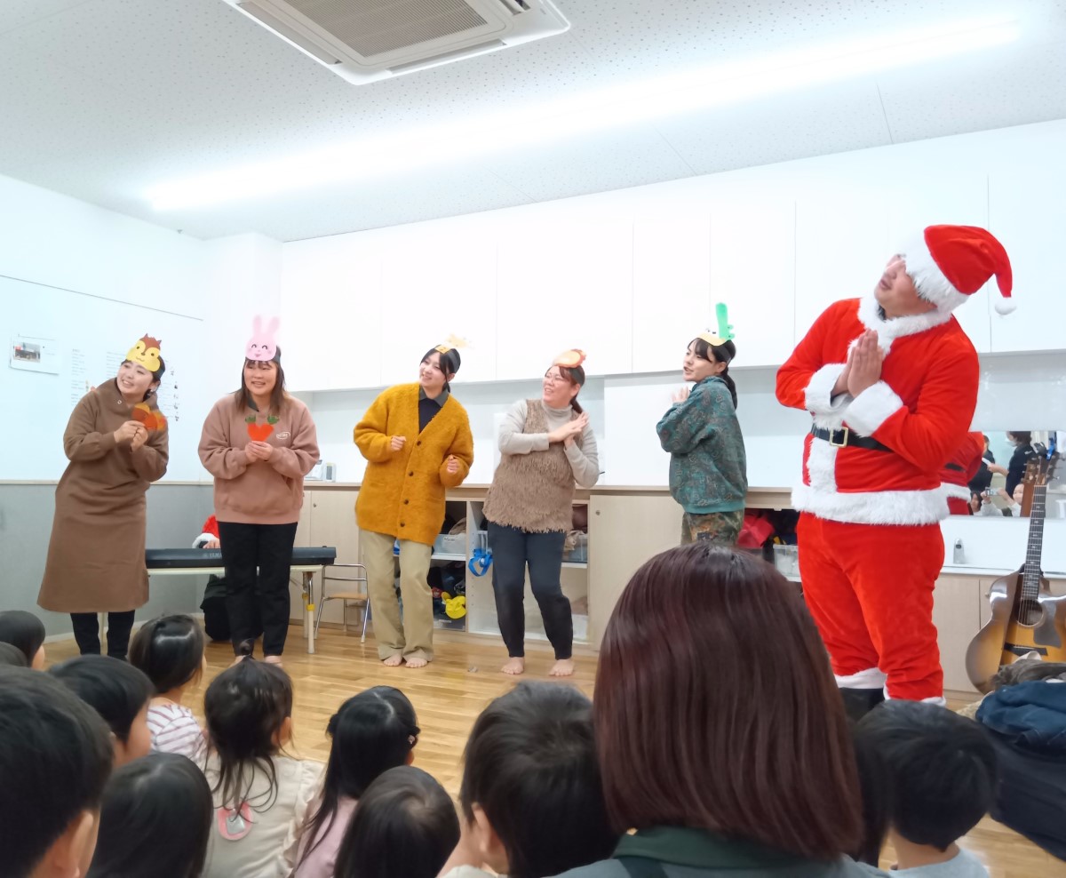動物のお面を付けた大人やサンタが歌う様子