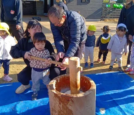 大人の手を借りながら餅をつく子ども
