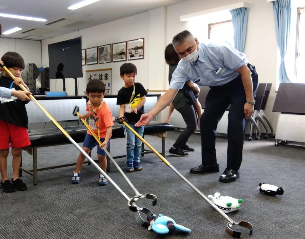 マジックハンドで落とし物を拾う体験をする子どもたちを