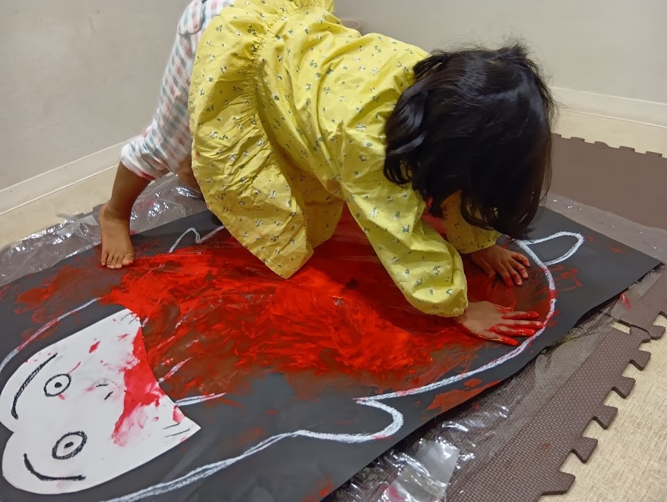 大きなだるまの絵に両手で絵の具を付ける子ども