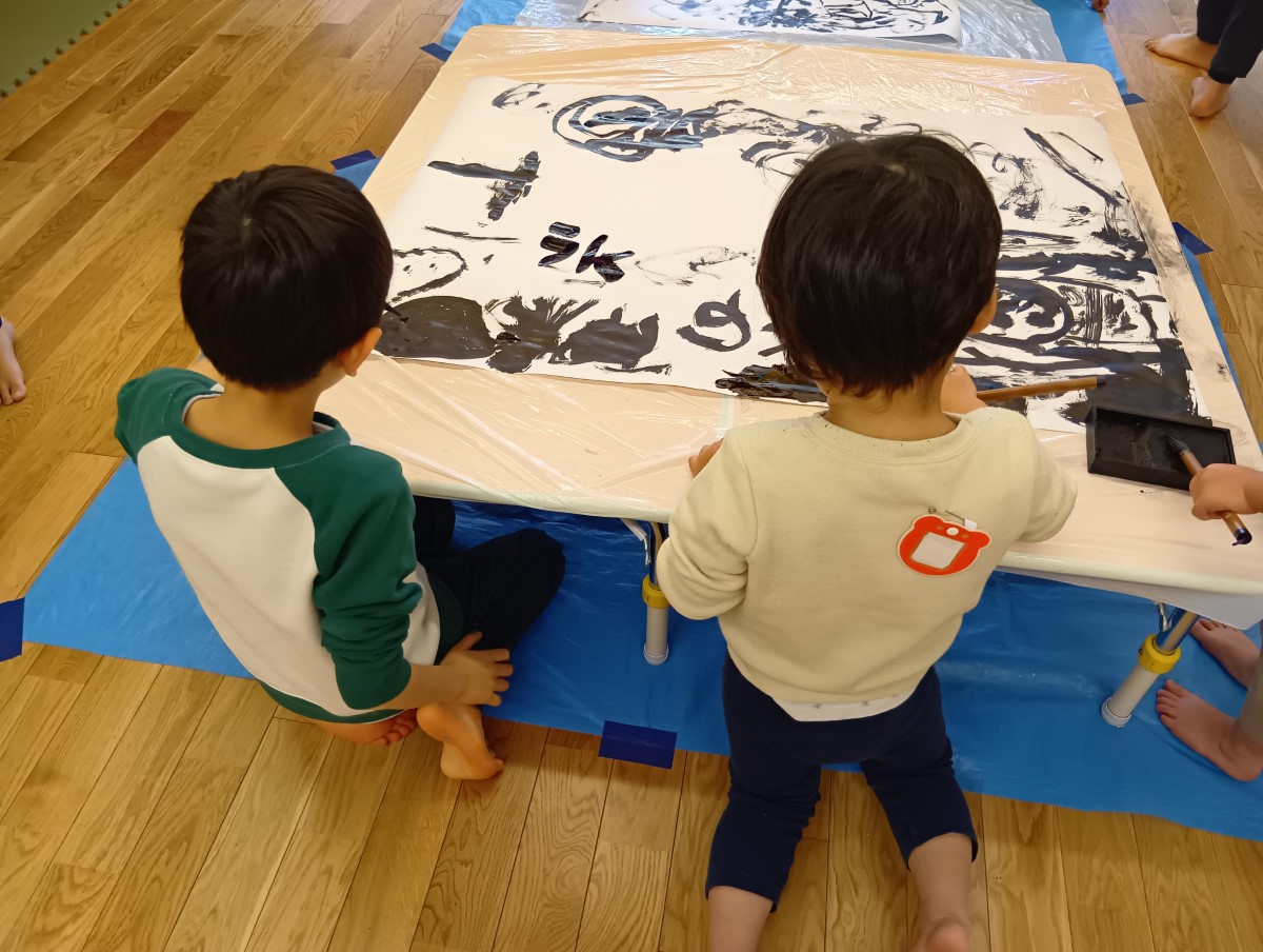 机の上の模造紙に墨で絵を描く子どもたち