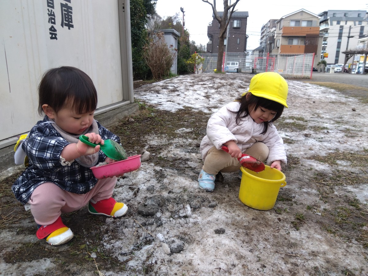 スコップで雪交じりの土を集める子どもたち