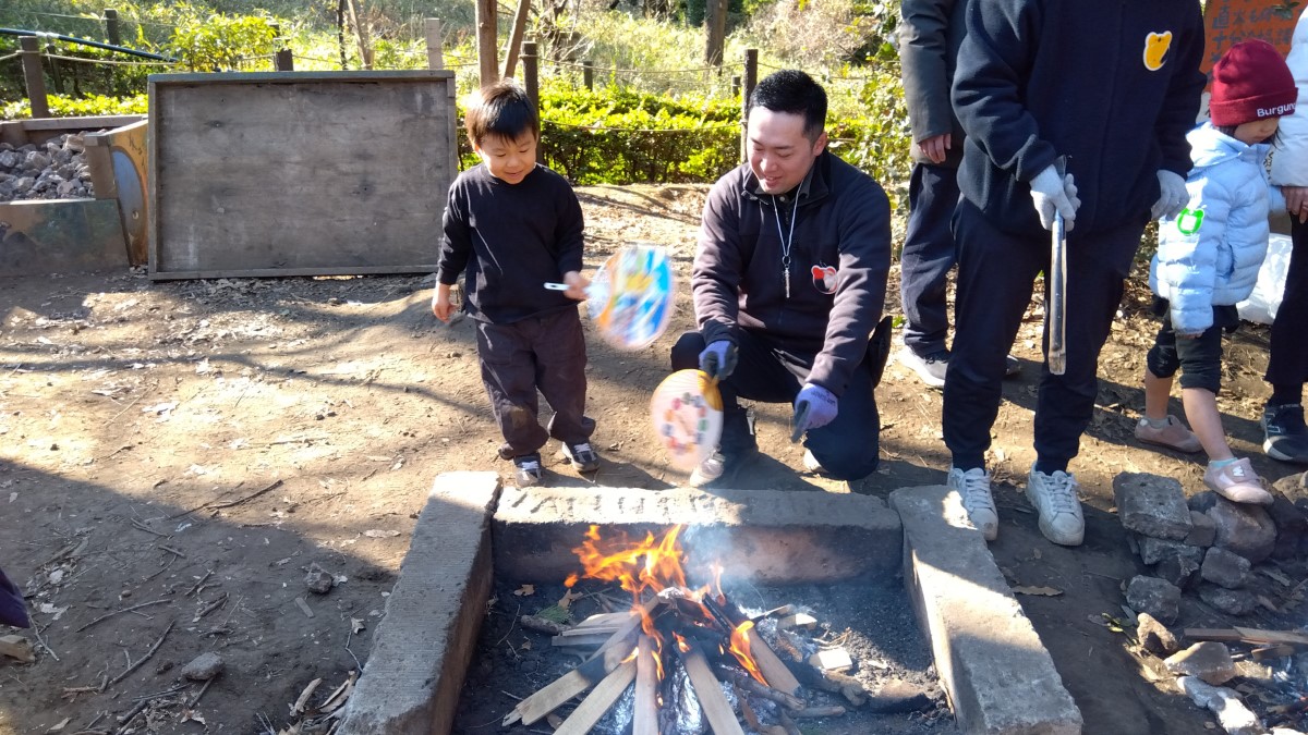 スタッフと一緒にうちわで焚き火に風を送る子ども