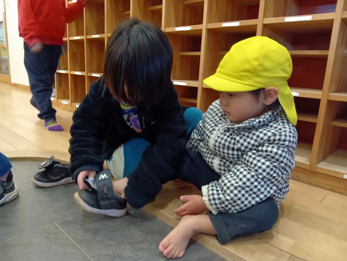 年下の子に靴を履かせてあげる子どもの様子