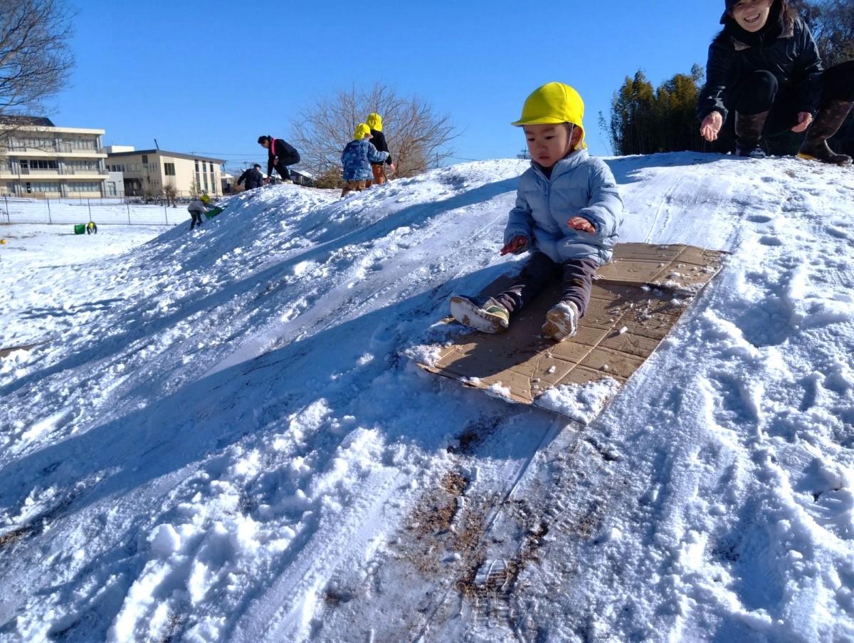 築山でそり遊びをする子ども