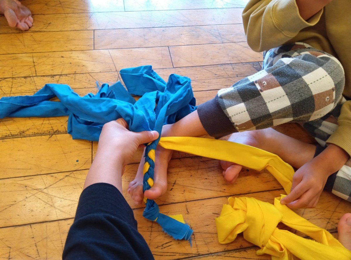 手足を使って布記事を三つ編みにする子ども