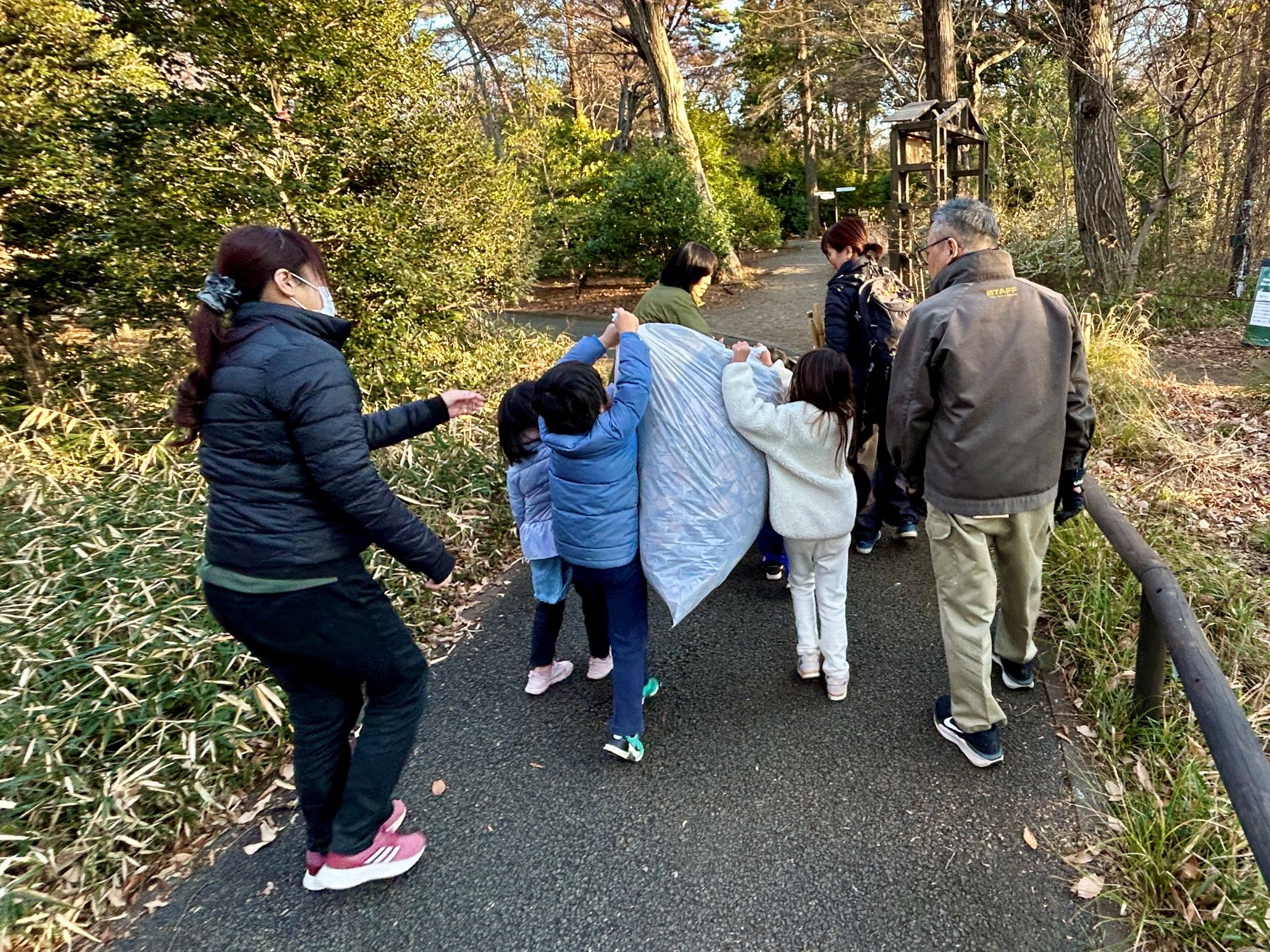 子ども3人がかき集めた大きな落ち葉の袋を持ち上げて運ぶ様子