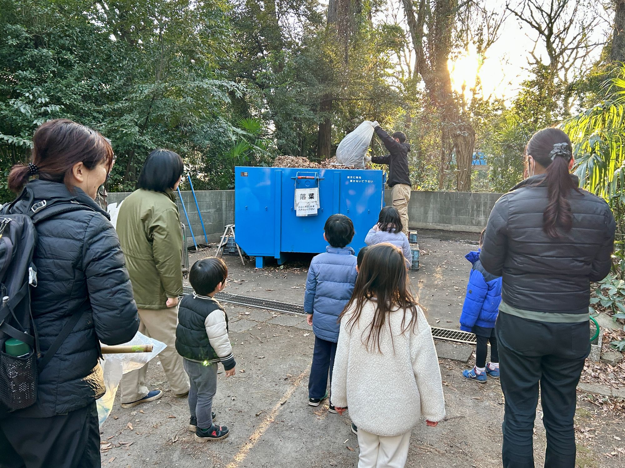 職員が、みんなで集めた落ち葉を所定の集積箱に入れる様子