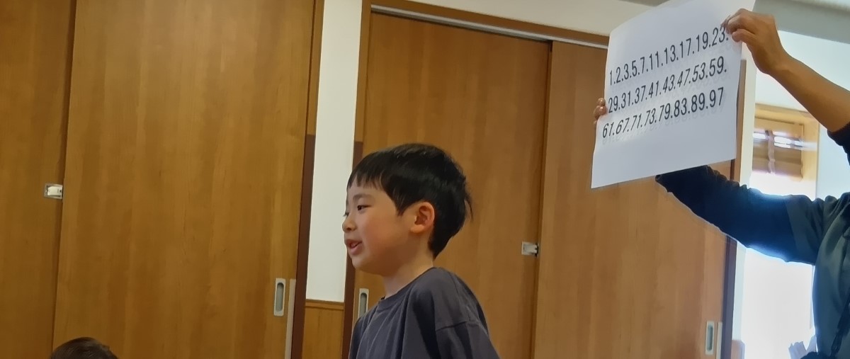 素数の一覧が書かれた紙を背にする子ども