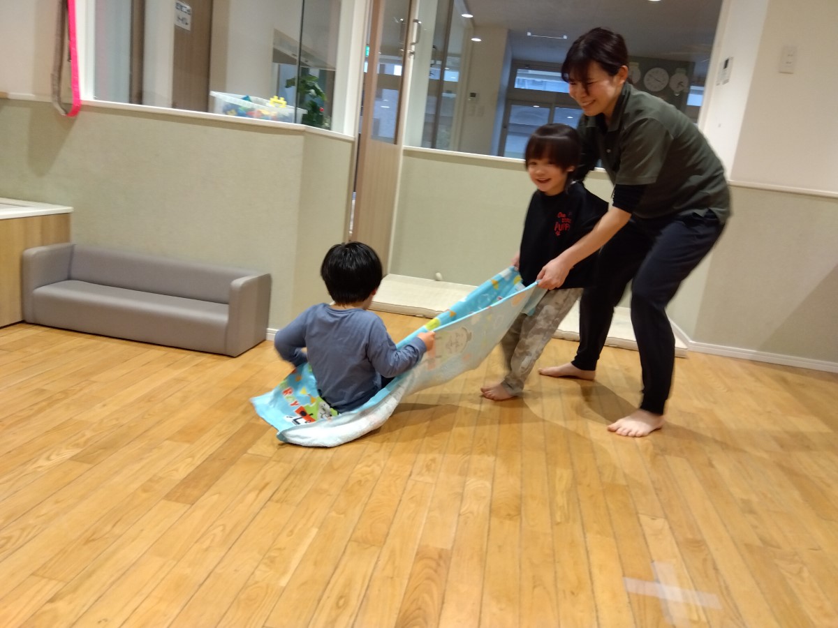 子どもが乗ったタオルをスタッフと子どもが引っ張って遊ぶ様子