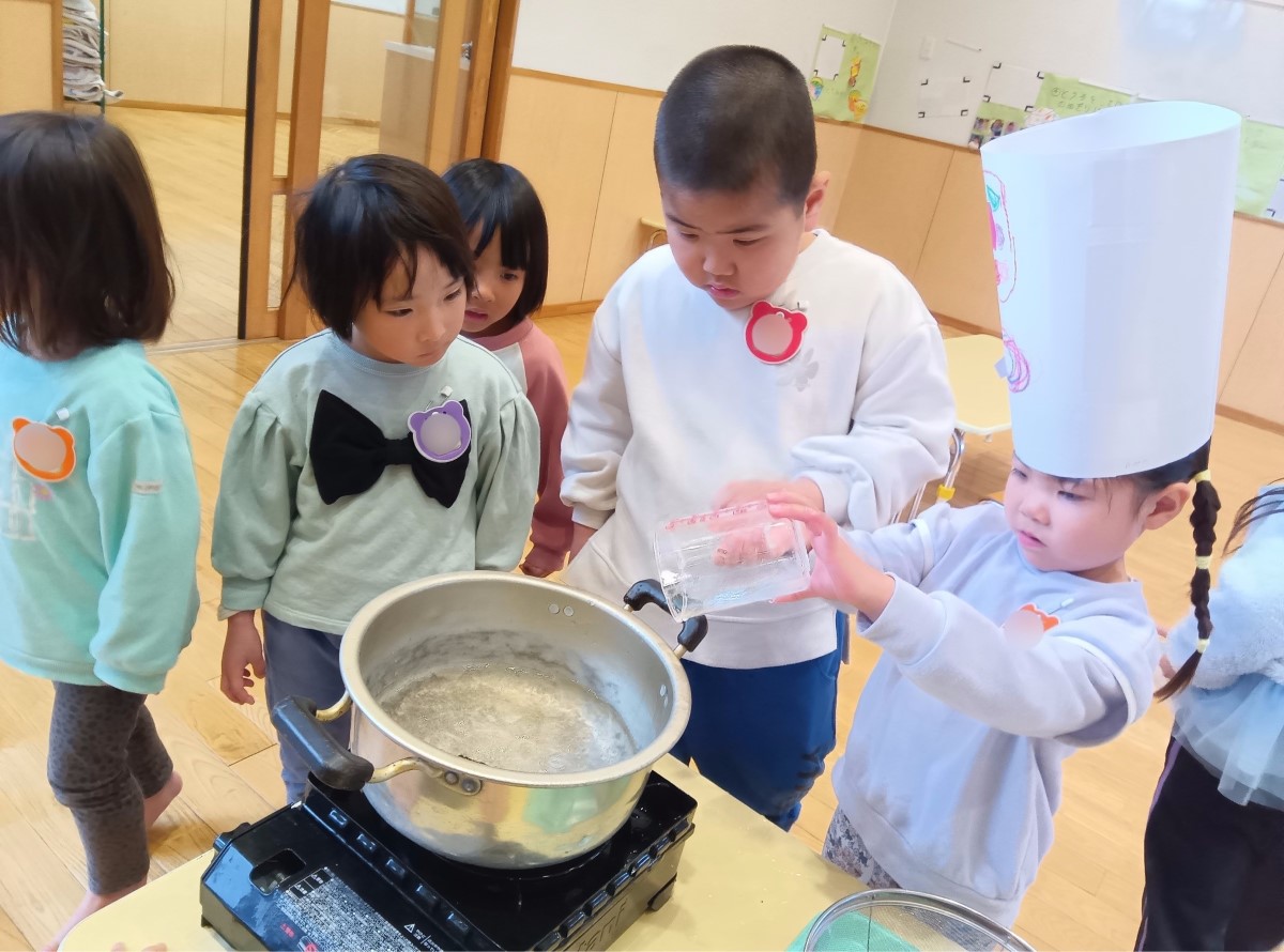 大きな鍋に水を入れる子ども