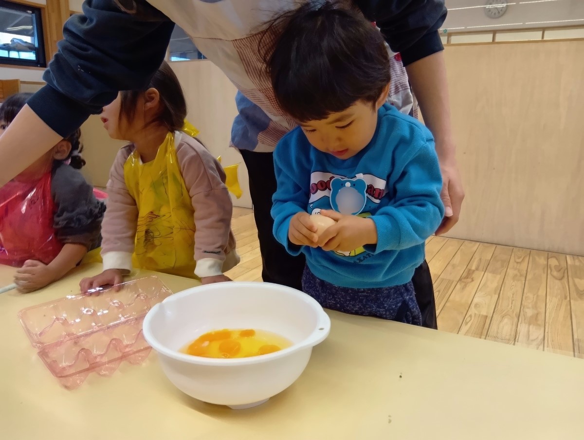 ボウルに卵を割り入れる子ども