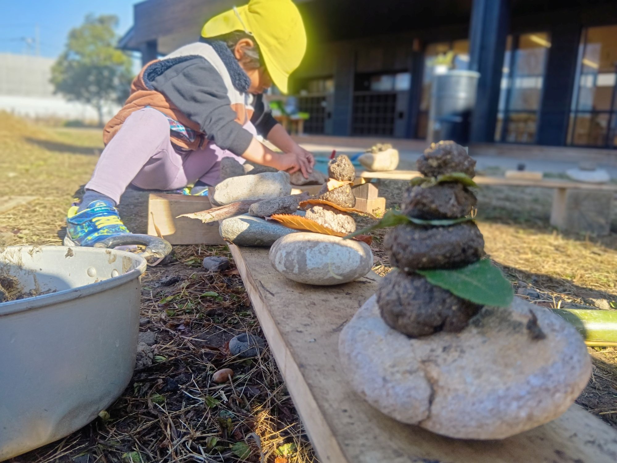 園児が園庭に配置されたどろや石などの自然素材で遊ぶ様子