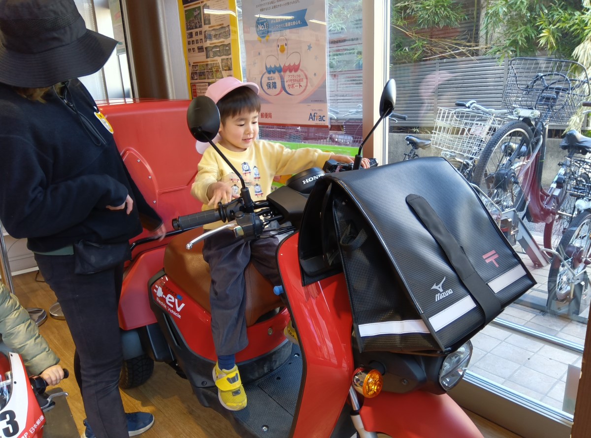郵便バイクに座らせてもらう子ども